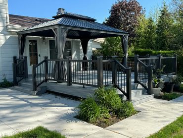 Modern backyard deck with a metal gazebo and black railings.