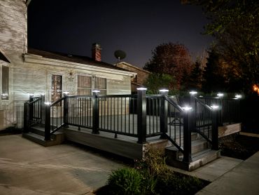 Illuminated backyard deck with railing at night.