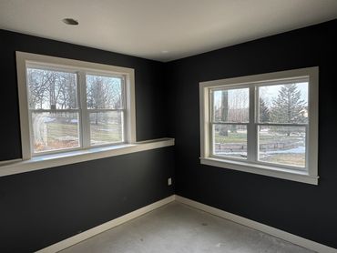 Empty room corner with black walls and two white-framed windows.