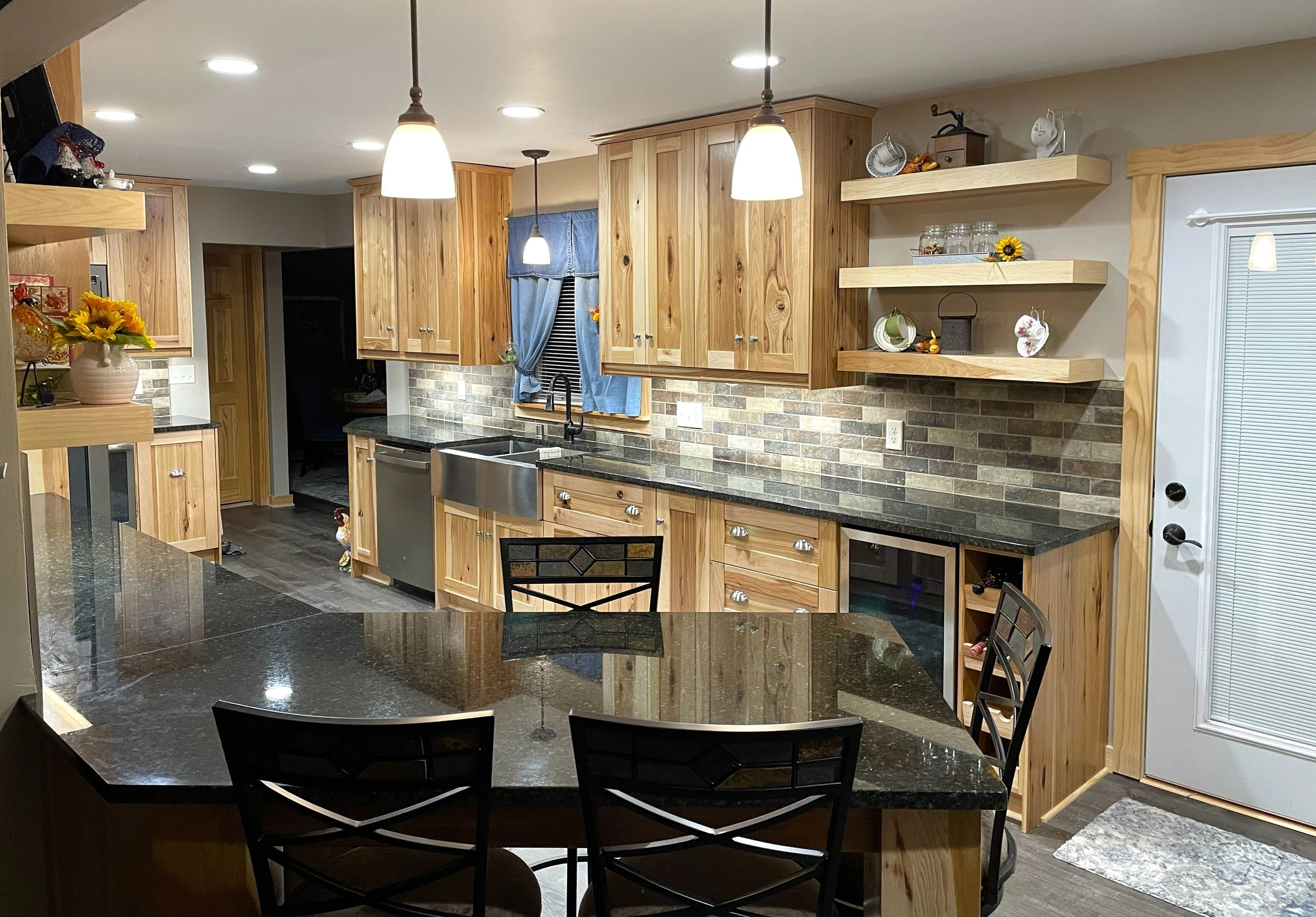 Modern kitchen with Hickory wood cabinets, tile backsplash, black granite countertops, and pendant l