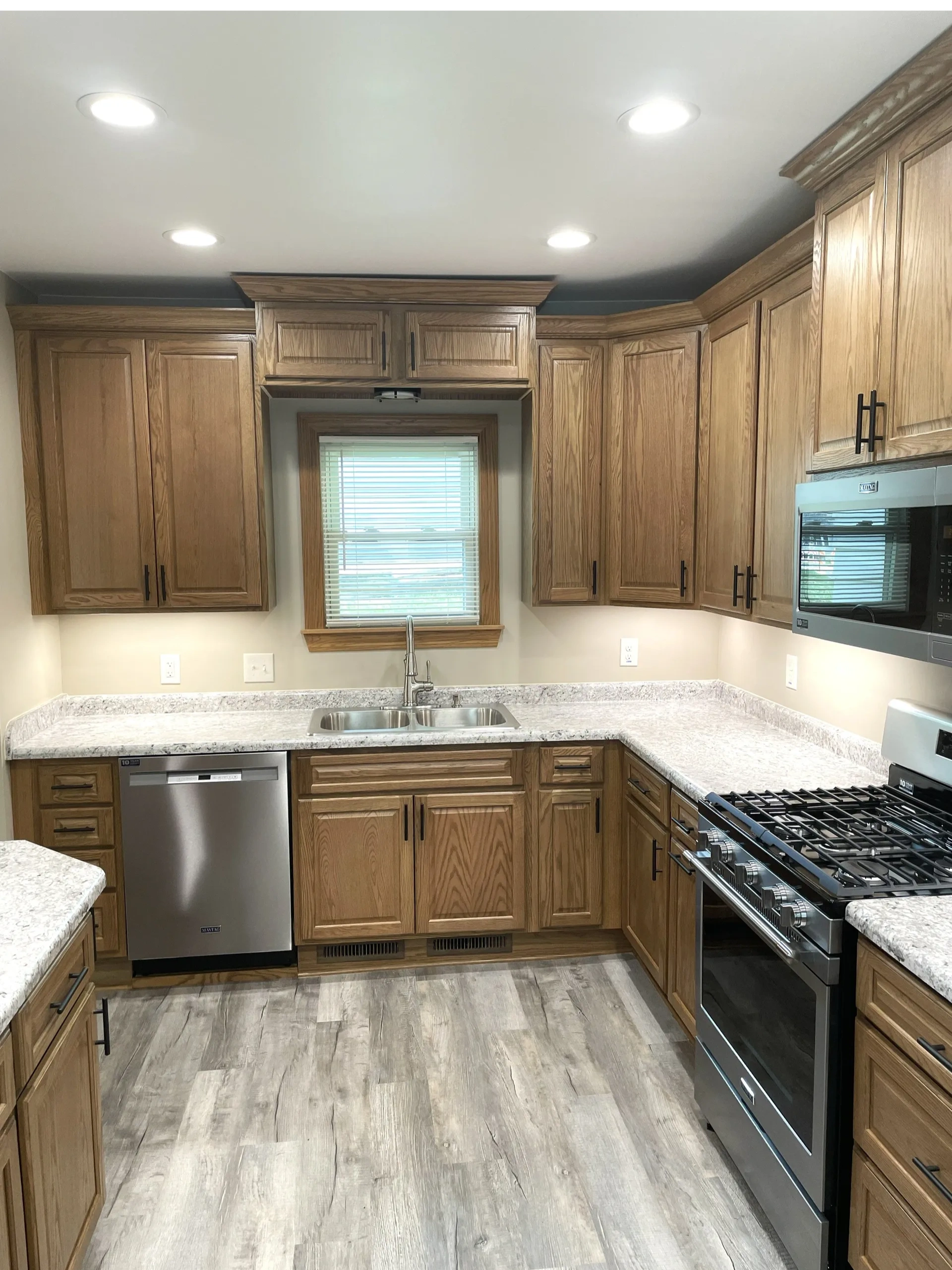 Modern kitchen with wooden cabinets, stainless steel appliances, and light granite countertops.