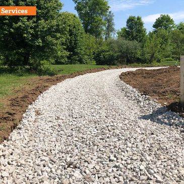 Newly laid gravel driveway bordered by wooden gates and greenery.