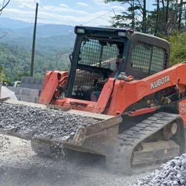 Kubota skid steer spreading gravel from a truck for installation services.