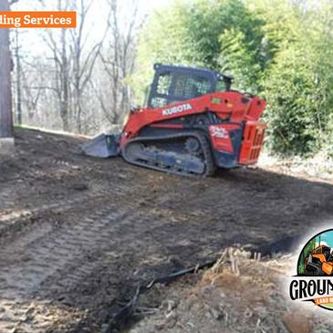 Red Kubota bulldozer grading land in a wooded area.
