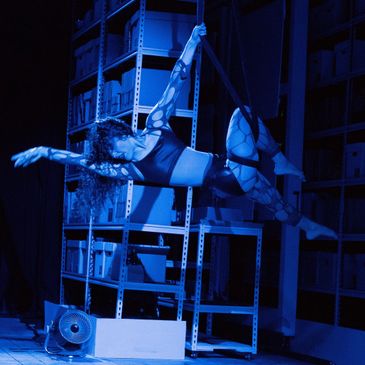 Renee performs on aerial rope sling in blue light. 