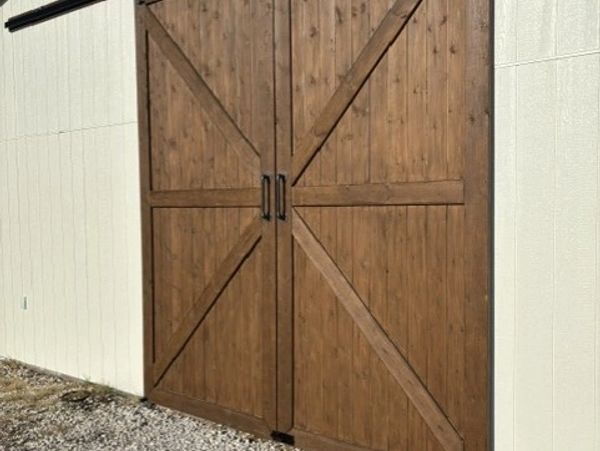 Rustic wooden barn doors with metal handles on a white building.