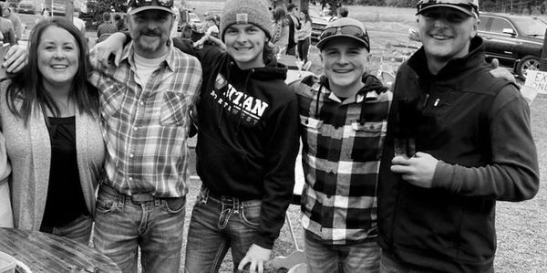 A happy group of five people smiling outdoors in casual clothes.