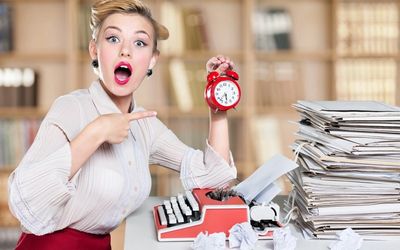 A woman surrounded by piles of paper pointing to a clock in her hand.