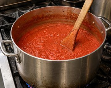 Simmering pot of tomato sauce with wooden spoon.