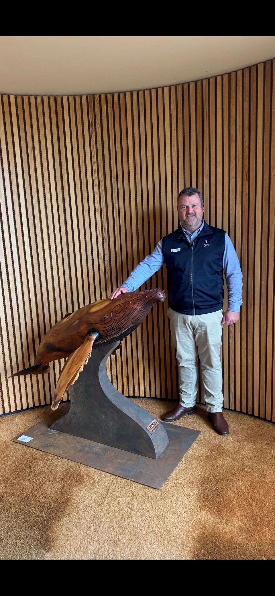 Man standing beside a wooden whale sculpture.