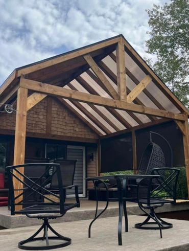 Wooden pergola with patio furniture under a cloudy sky.