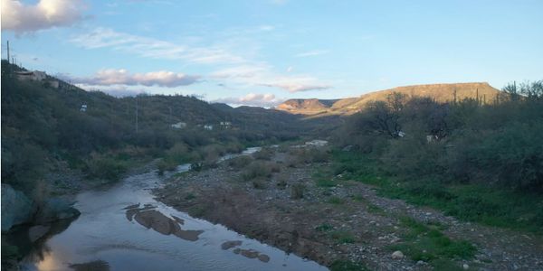 A calm river flowing through a hilly, green landscape under a blue sky.