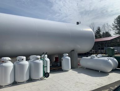 Large and small white propane tanks stored outdoors under a partly cloudy sky.