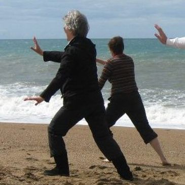 Two people practicing tai chi on a beach by the ocean.