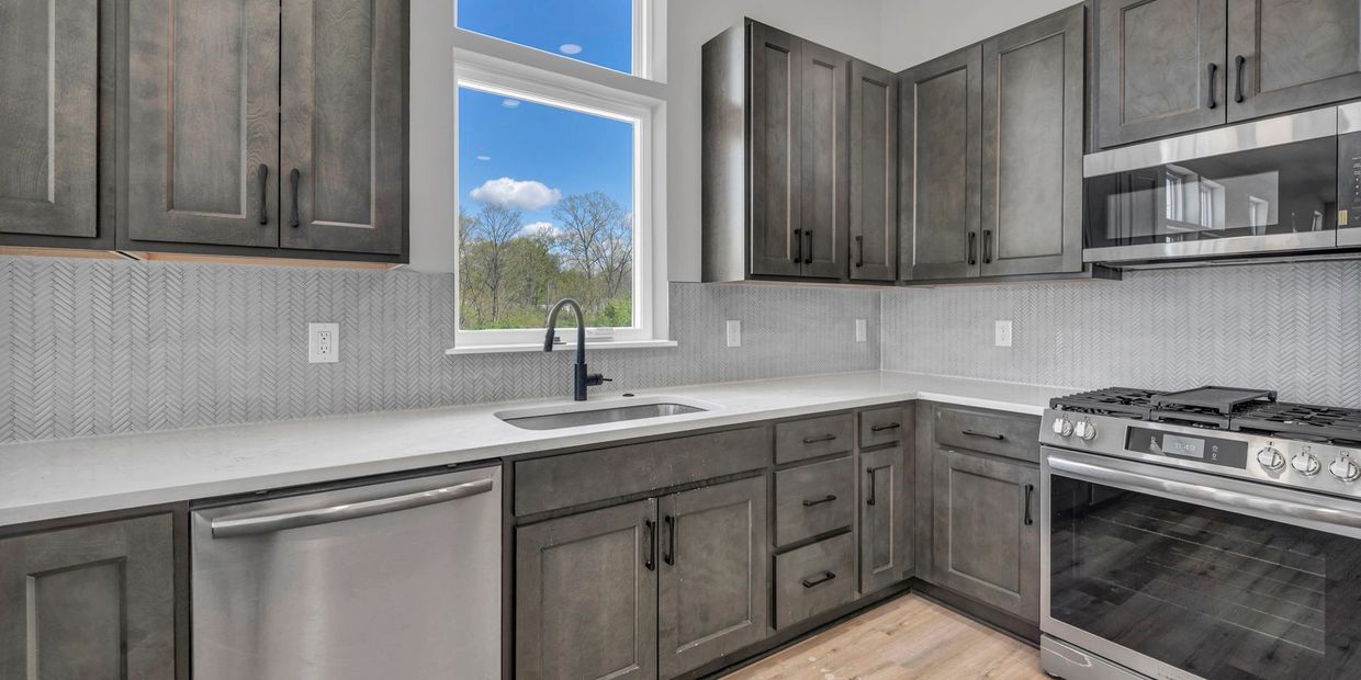 Modern kitchen with gray cabinets, stainless steel appliances, and a large window.