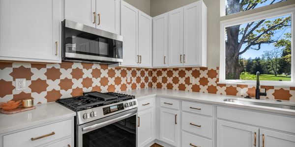 Modern kitchen with white cabinets and a patterned orange backsplash.