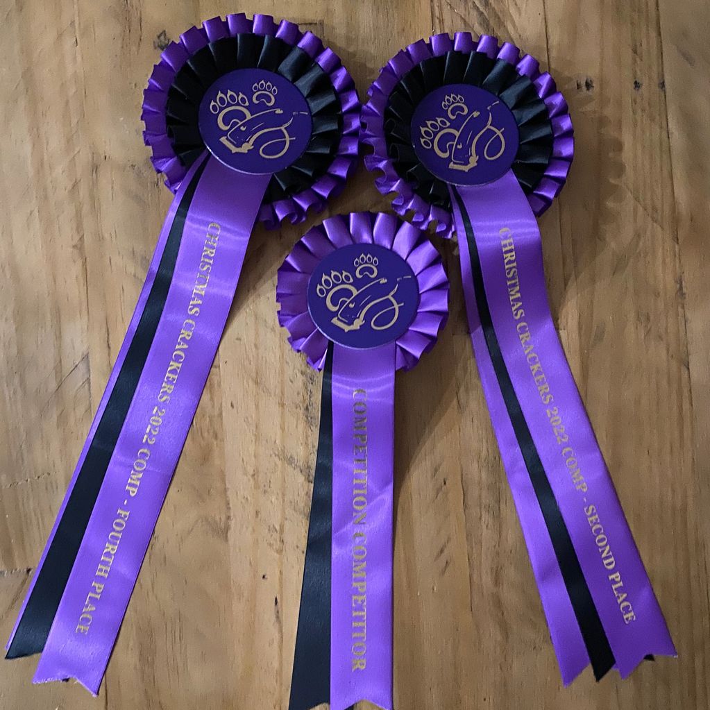 Three purple and black competition ribbons on a wooden surface.