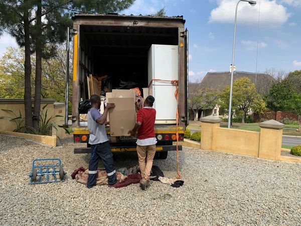 Two men unload boxes and a refrigerator from a moving truck.