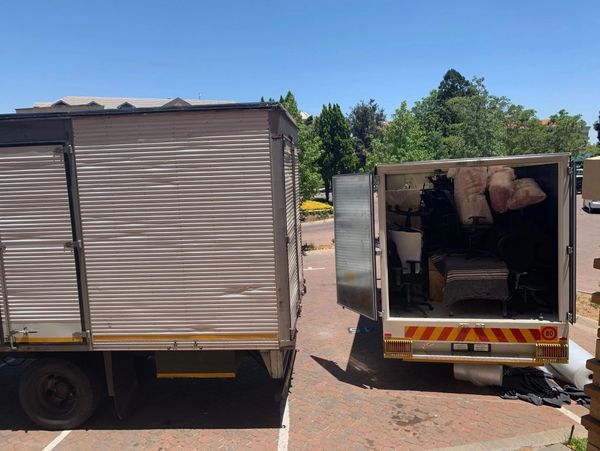 Two box trucks parked side by side, one with open rear door showing packed office chairs and wrapped items.