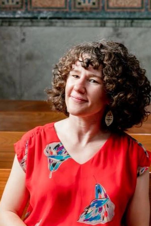 Woman with curly hair wearing a red butterfly-patterned blouse, smiling gently.