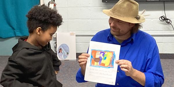 A man shows a colorful drawing to a young boy in a classroom.