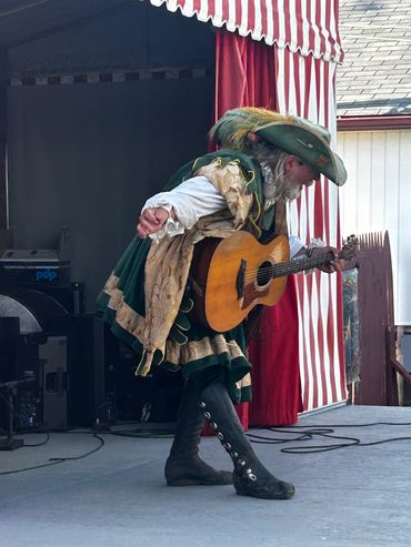 Man in renaissance costume playing guitar on stage.