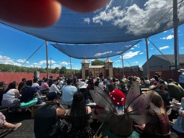 Crowd gathered outdoors under a canopy with fairy wings visible.