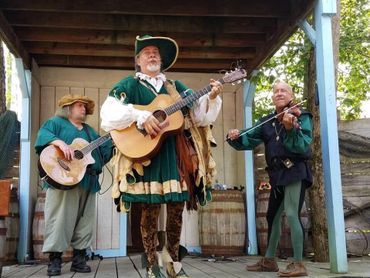 Three men in Renaissance attire playing musical instruments on a wooden stage.