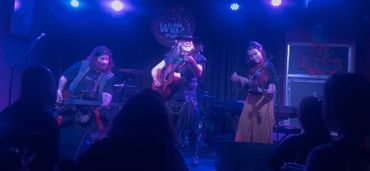 Three musicians perform on stage under blue lights with an audience watching.
