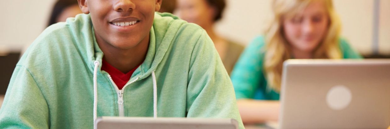 Smiling student using a tablet in a classroom setting.