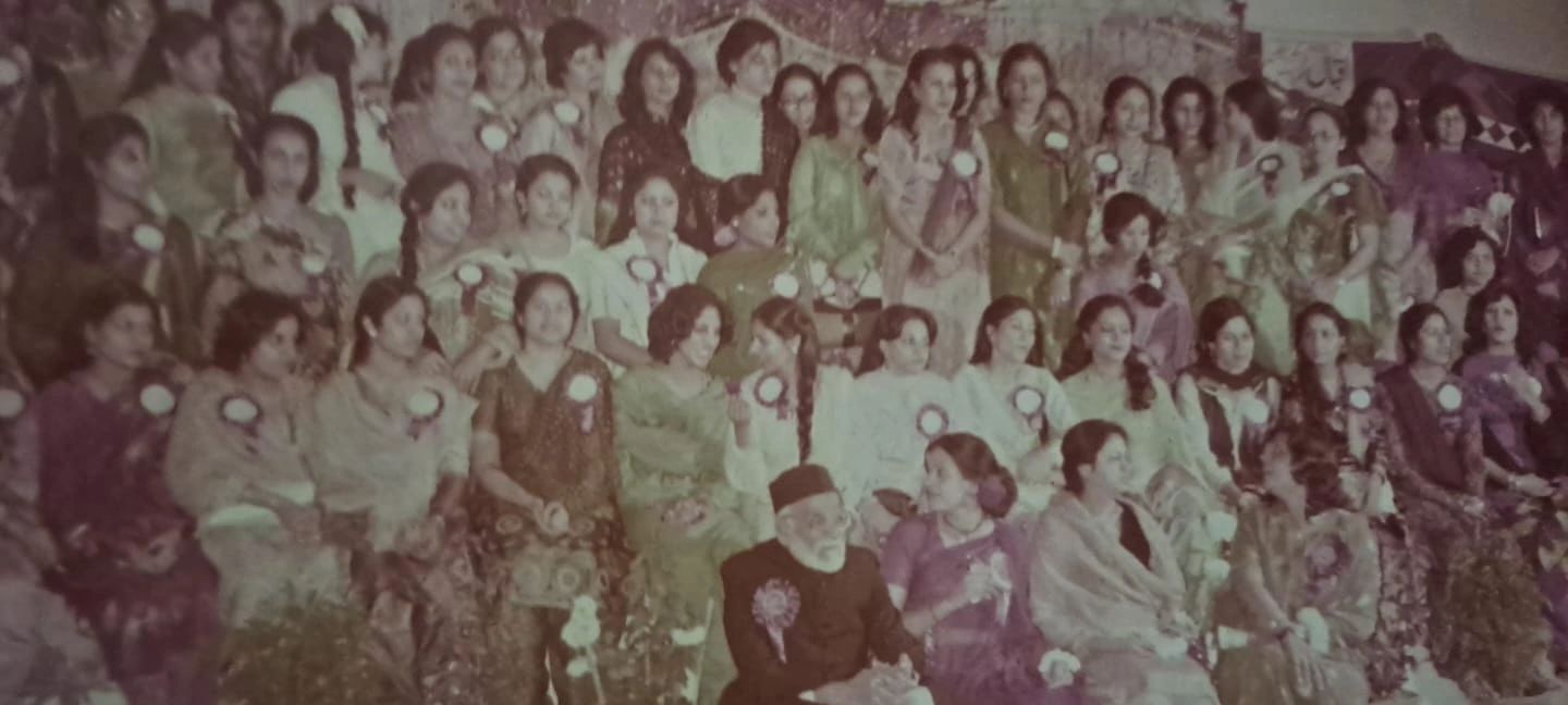 A large group photo of women and one man, all wearing badges, in traditional attire.