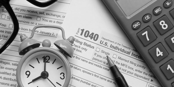 A clock, a Form 1040, a calculator, and a pen arranged on a table