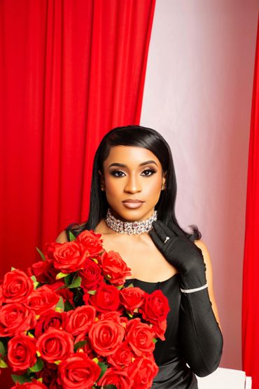 Elegant woman in black dress holding a bouquet of red roses against red and white backdrop.