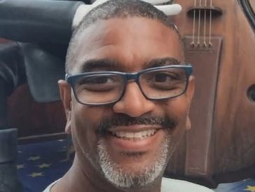 Smiling man with glasses and gray beard in front of a musical instrument.