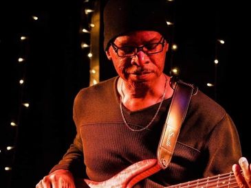 Man playing electric guitar under warm lighting with string lights in background.
