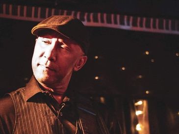 Man in a cap playing guitar on a dimly lit stage.