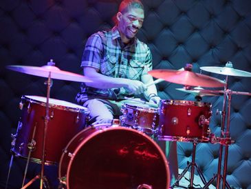 Man joyfully playing a drum set in a cozy music studio.