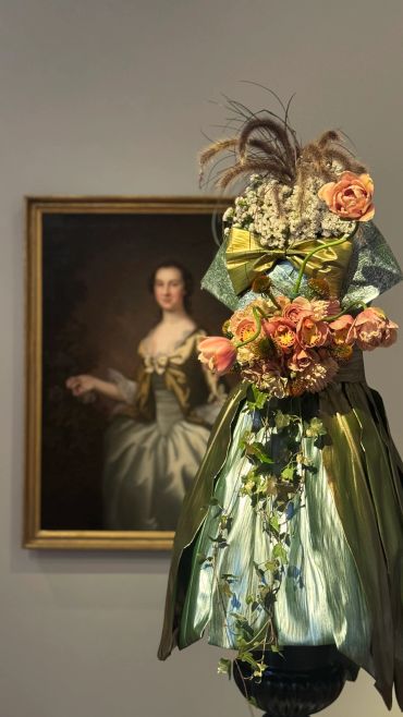 Decorative floral fashion display in front of a classical portrait.