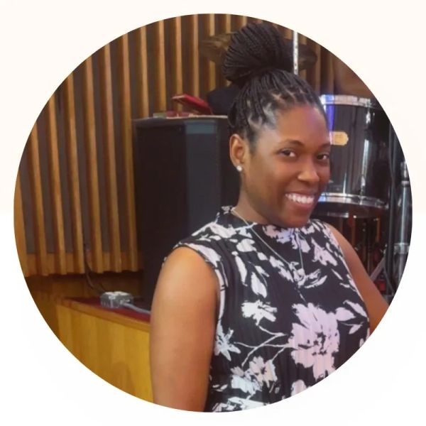 Woman smiling indoors with a drum set in the background.