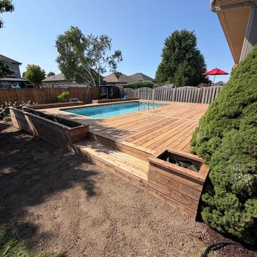 Backyard swimming pool with wooden deck and planter boxes.