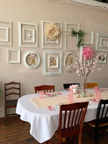 Elegant dining table with pink floral decor and vintage frames on the wall.