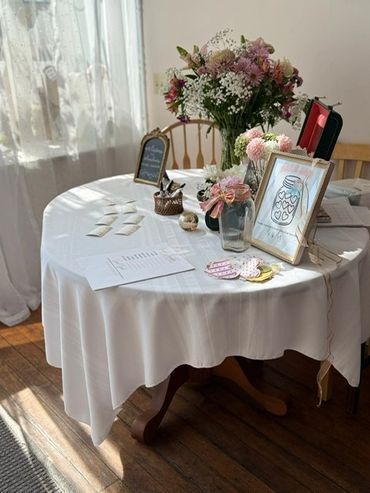 Decorated round table with flowers and wedding-themed items near window.