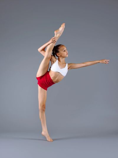 Young dancer in red shorts performing an impressive leg stretch.