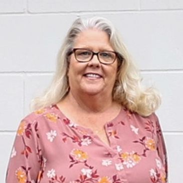 Headshot of a blond woman with glasses in a pink floral shirt