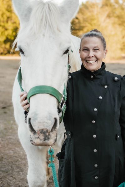 A lady smiling while holding a white horse