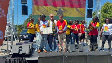 People standing on stage with Ghana flag in background.