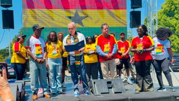 Group of people on stage with Ghana flag backdrop.