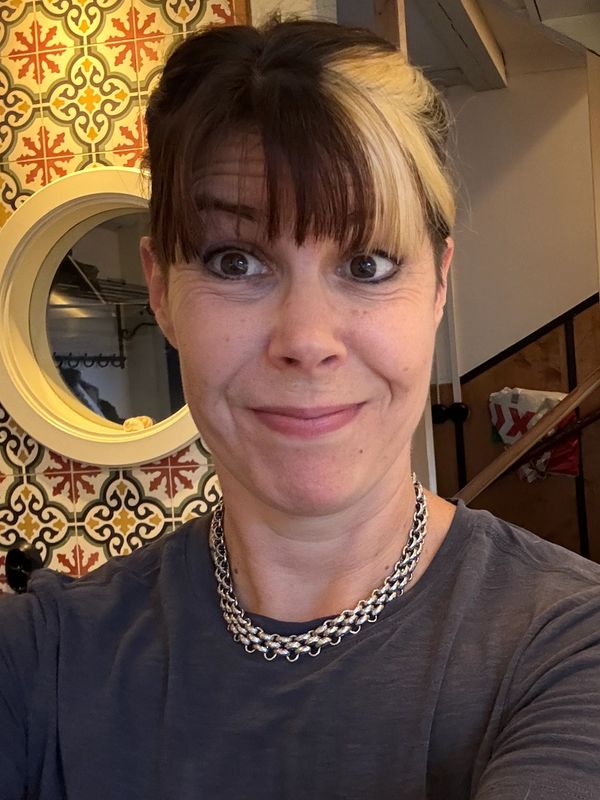 Woman with brown and blonde hair taking a selfie indoors with patterned wall.