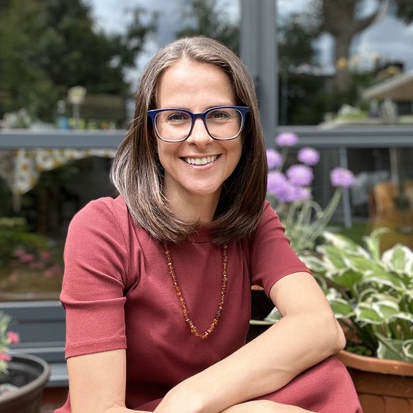 Photo of Kath Murray sitting in a garden wearing a burnt orange dress arms folded over knees