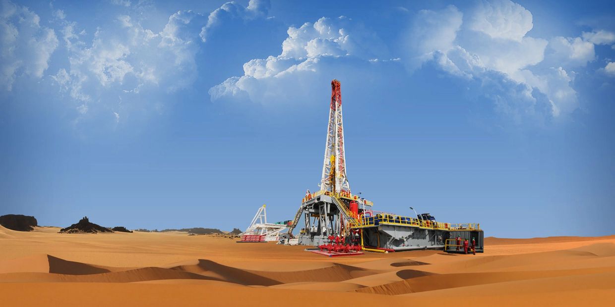 Oil drilling rig stands tall in a vast desert under a bright blue sky.